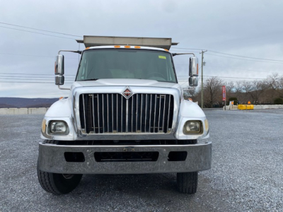 International 7400 dump truck front view showing grille, bumper, headlights, and large silver bumper in a gravel lot.