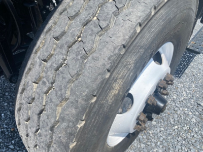 Truck wheel and tire close-up showing hub with lug nuts; tread pattern visible on tire; part of suspension and frame visible.