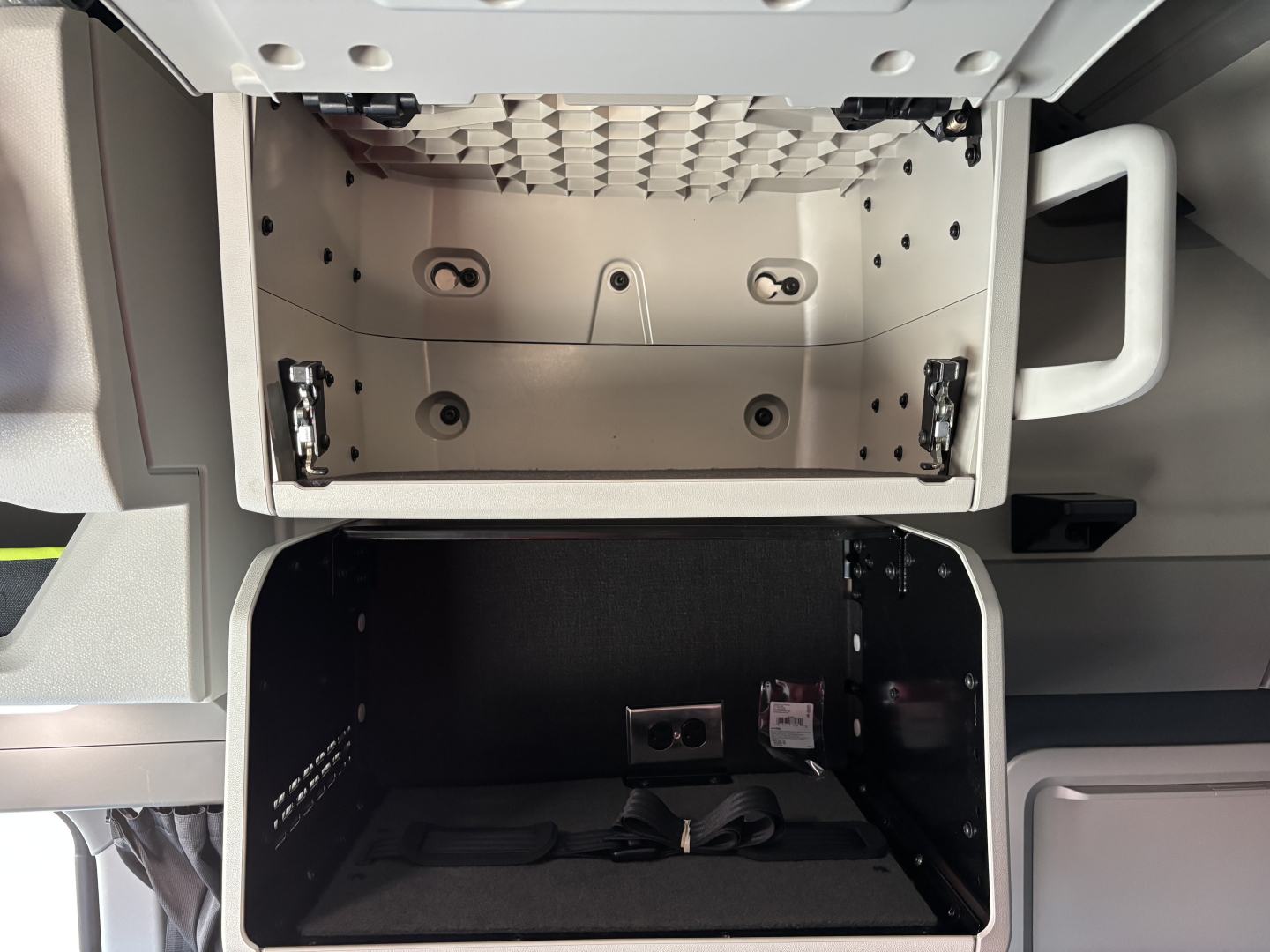 Volvo VNL64T860 cab interior showing an open upper bunk storage area and lower storage compartment with seating/strap components.