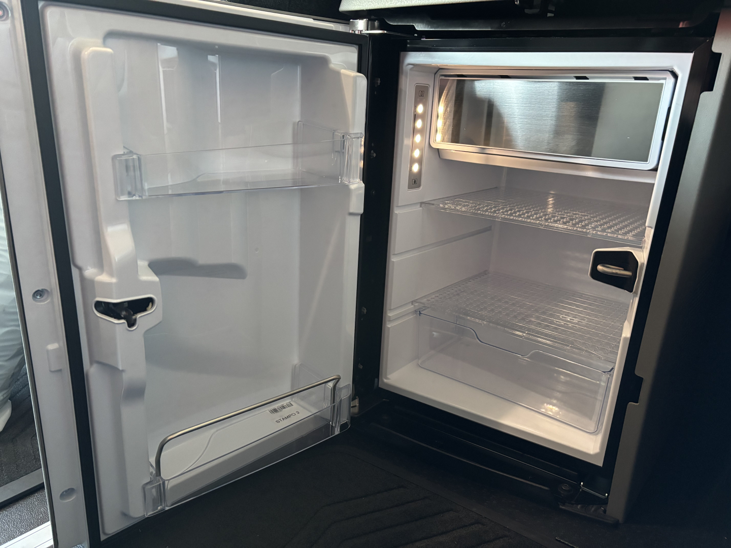 Volvo VNL64T860 truck sleeper cab interior showing a compact fridge/freezer unit with shelves and LED lighting and empty interior.