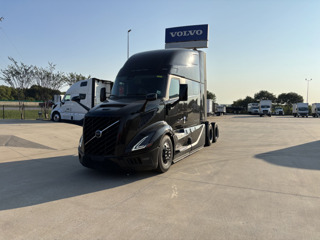 Volvo VNL64T860 semi truck in a dealership lot showing a sleek black exterior and Volvo sign above in background.