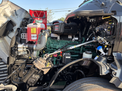 Volvo VNL64T860 engine bay showing green engine block and various components including red coolant reservoir, hoses, and wiring harnesses.
