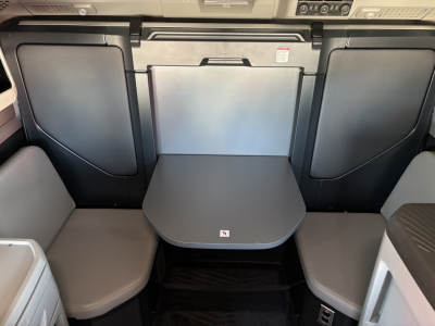 Volvo VNL64T860 interior seating area with fold-down table between two captain seats, dark gray panels, and storage compartments.