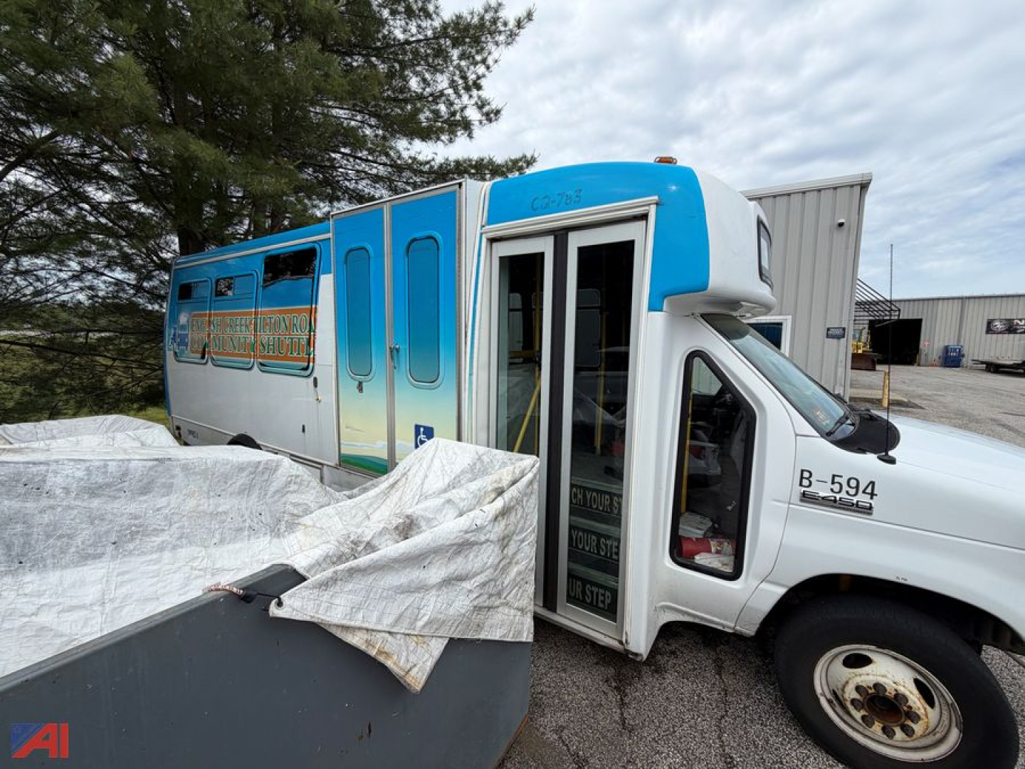 Bus interior and exterior of a 2016 Ford E450 shuttle bus with blue and white paint, open front passenger door, B-594 on the cab, parked near a warehouse.
