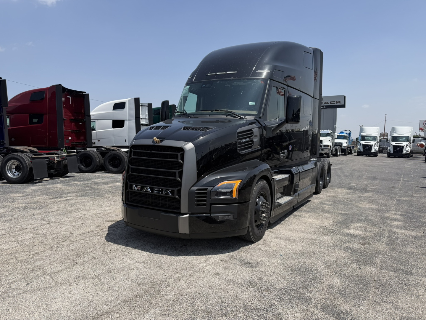 Mack PR64T76H conventional sleeper truck in black front view showing aerodynamic hood and grille and daytime running headlights.