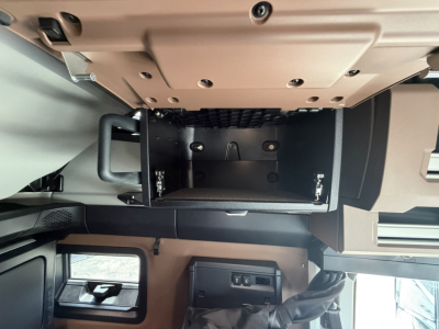 Truck sleeper cab interior showing open overhead storage compartment with empty tray and nearby control panel area.