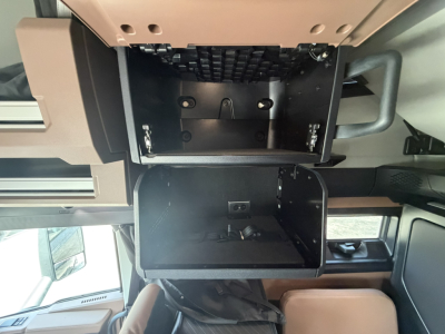 Cab interior showing storage compartments and dash area in a Mack PR64T76H truck, with open under-dash drawer and exposed mounting points.