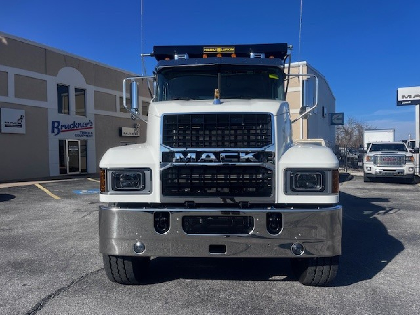 Front view of a white 2026 Mack PI64 dump truck showing large grille with MACK lettering, bumper, and headlights; includes stock number 69214 and dealership backdrop.