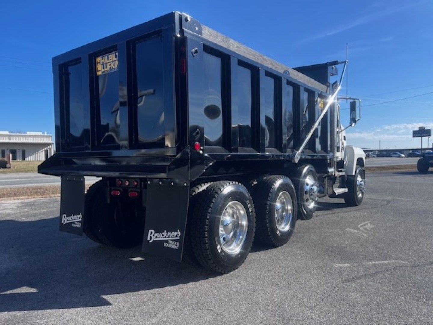 Dump truck chassis showing a black Mack PI64 dump bed with triple rear axles and chrome wheels, rear view of cab, stock number 69214.