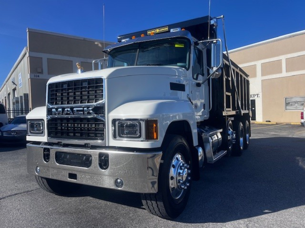 Mack PI64 dump truck showing front grille with Mack emblem and chrome bumper; headlights; white cab; side mirrors; front wheel; reflective surfaces.