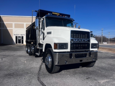 Dump truck front three-quarter view showing 2026 Mack PI64 with white cab, black grille, chrome bumper, and dual rear axles.