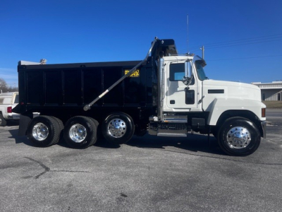 Dump truck in serviceable condition showing Mack PI64 cab with black dump body, chrome wheels, side step, and hydraulic dumping mechanism.