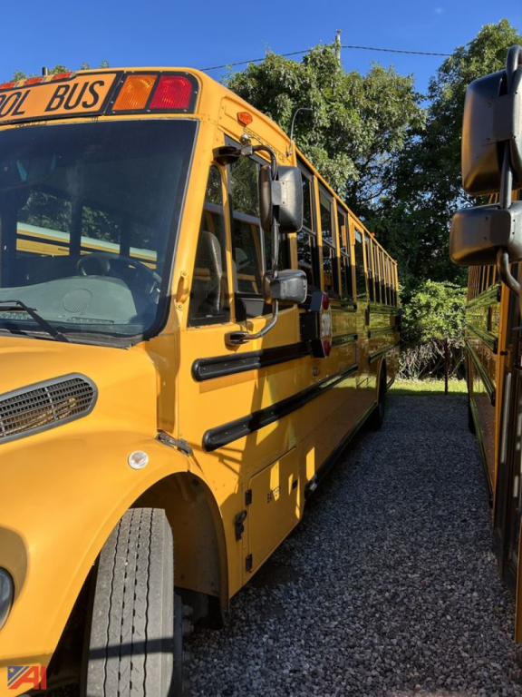 Bus body showing side of yellow Freightliner B2B school bus with black trim; front wheel, door, and side windows visible