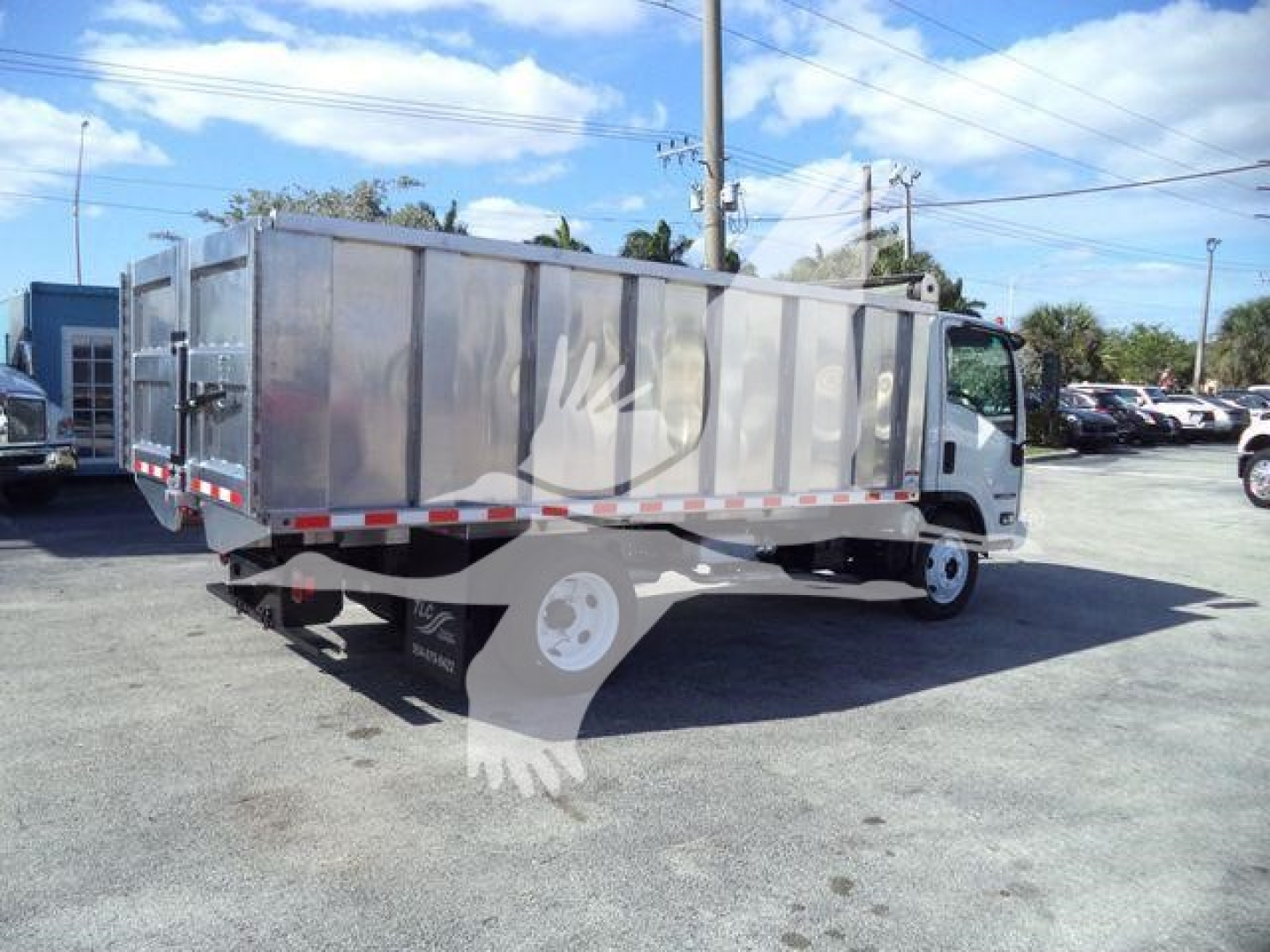 Isuzu NPR HD dump truck in a parking lot, side view showing a large metal dump bed and white cab with black tires; no legible serials or labels visible on body.