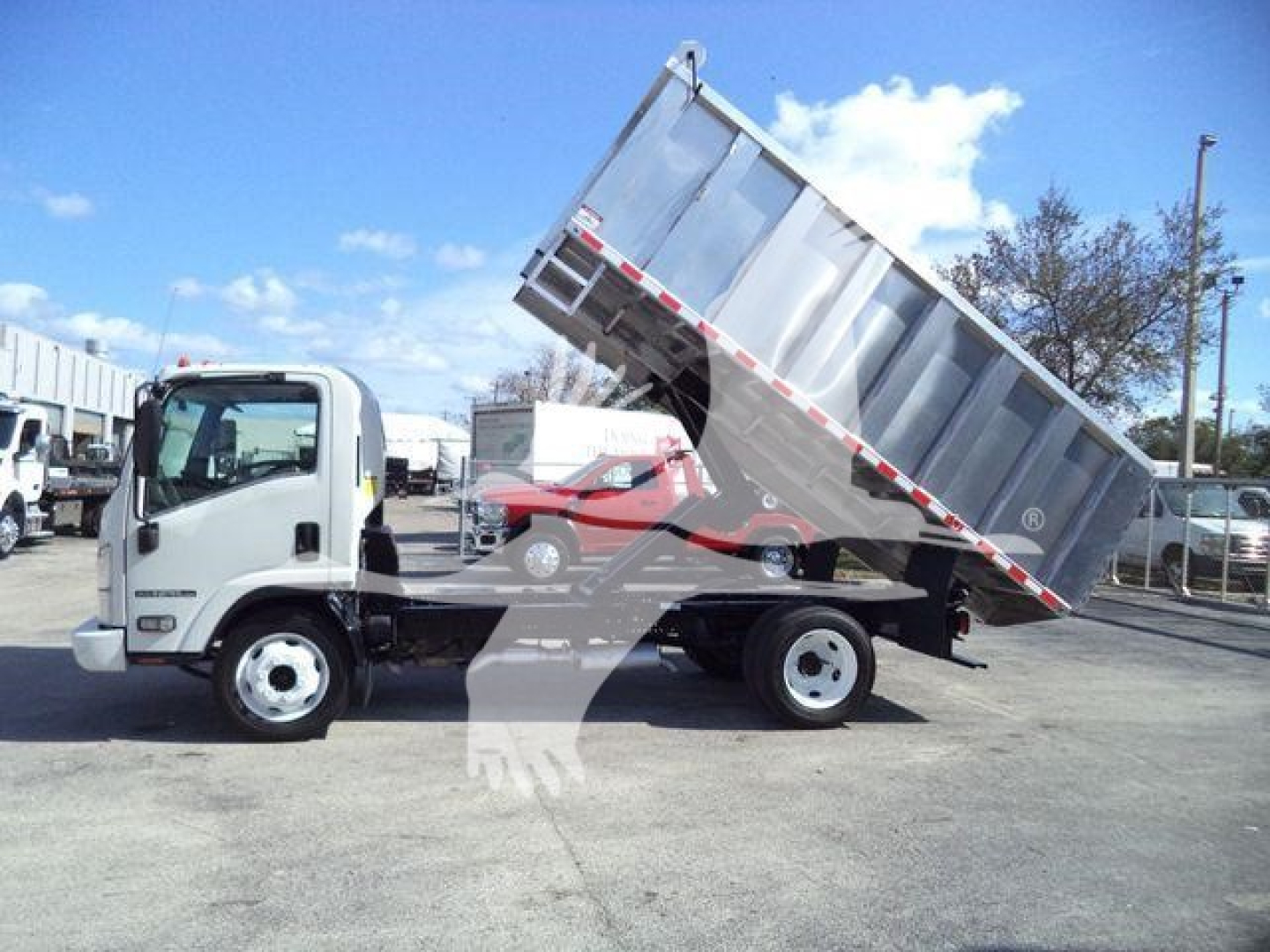 Isuzu NPR HD dump truck showing tilted cargo bed in landscape view with white cab and silver dump body.