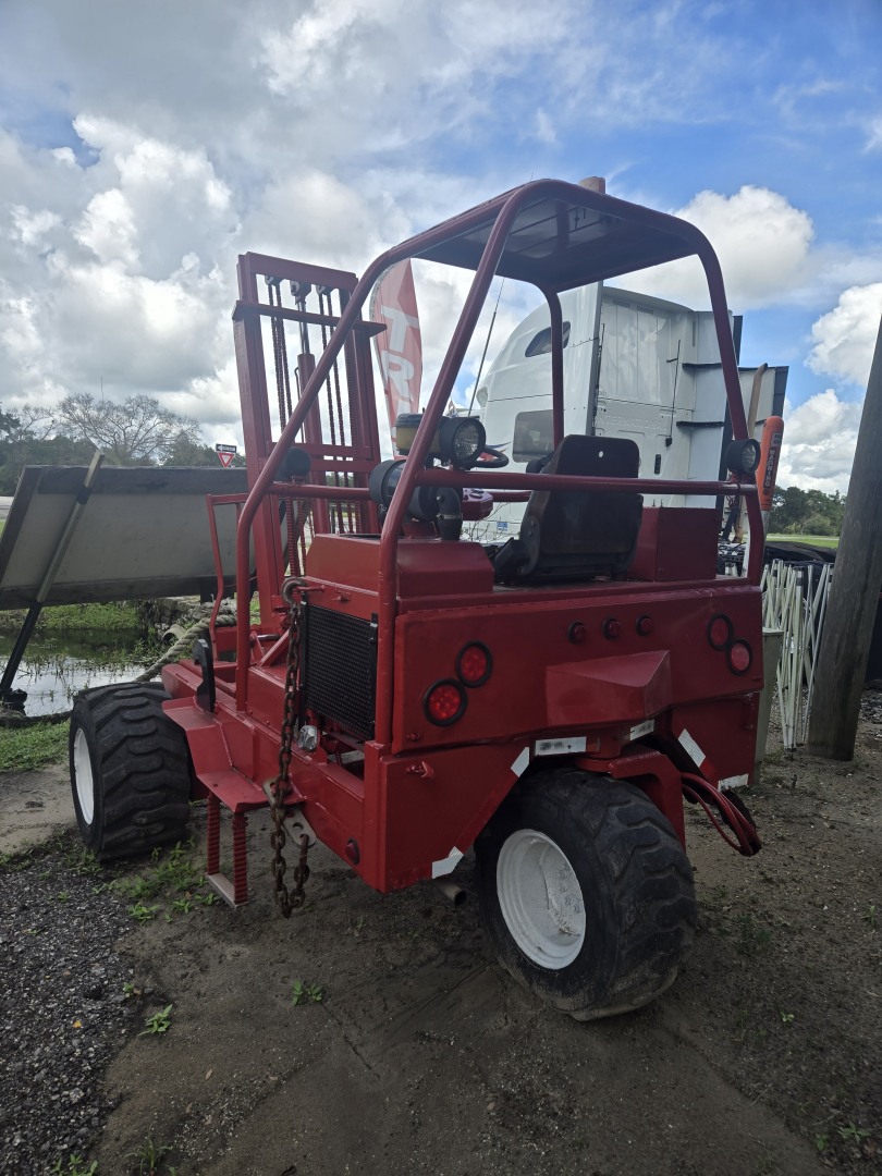 Forklift-like vehicle in red with a roll cage and two seats, rear view showing large off-road tires and chains, used telescopic lift equipment.