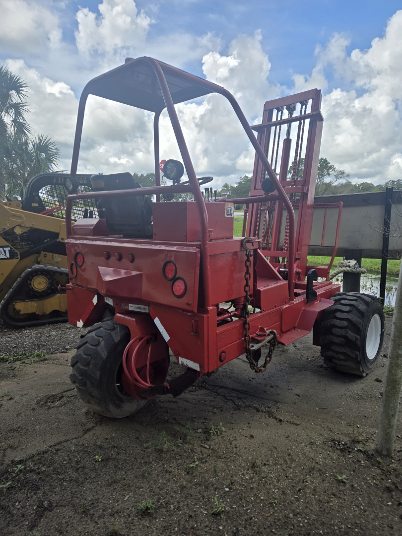 Equipment: 2012 piggyback lift showing red frame, open operator cab, large off-road tires, hydraulic hoses, and lifting framework.