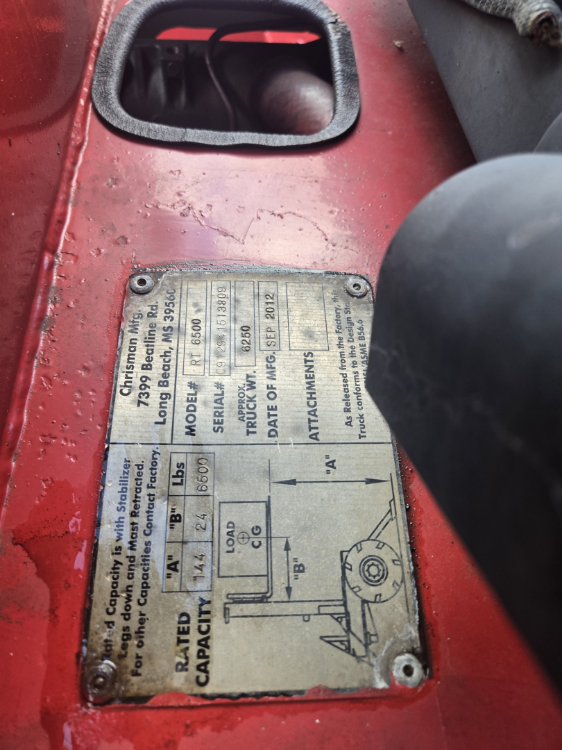 Plate on red telescopic lift showing specifications: wheelbase, capacity, model, serial, attachments; label with diagrams and text, screws at corners.