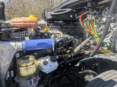 Engine bay of a 2022 Freightliner Cascadia 126 showing coolant reservoir, power steering fluid reservoir, air intake, and various colored wiring harnesses.