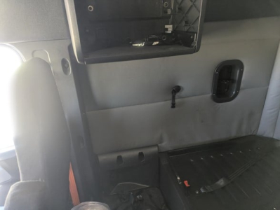 Truck interior view showing a dashboard cutaway and open storage compartment in a Freightliner Cascadia sleeper cab dash area with wiring and a black handle recess.