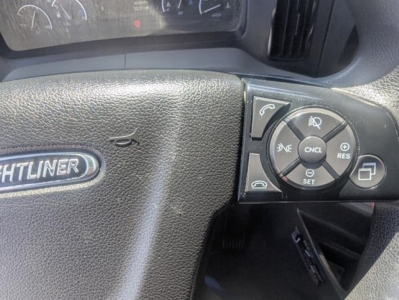 Steering wheel area of a 2022 Freightliner Cascadia 126 showing cruise control cluster on the right side of the steering wheel and part of the dashboard with the 'Freightliner' badge.