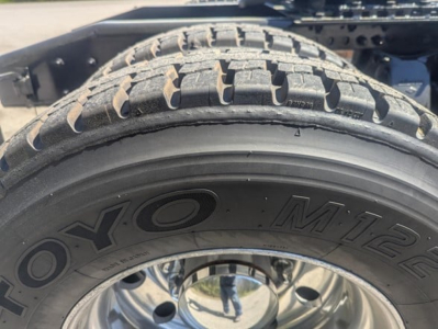 Tire with 'TOYO M+S' sidewall and wheel reflection; part of Freightliner Cascadia truck chassis visible above.