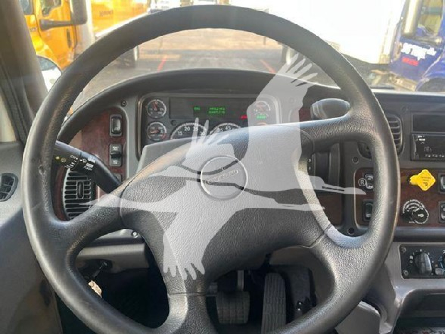 Steering wheel inside a Freightliner M2-106 cabin showing gauge cluster, pedals, and dashboard controls.