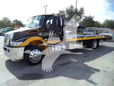 Tow truck with black and yellow color scheme, flatbed rollback on a lot. Visible text includes none legible on panels.