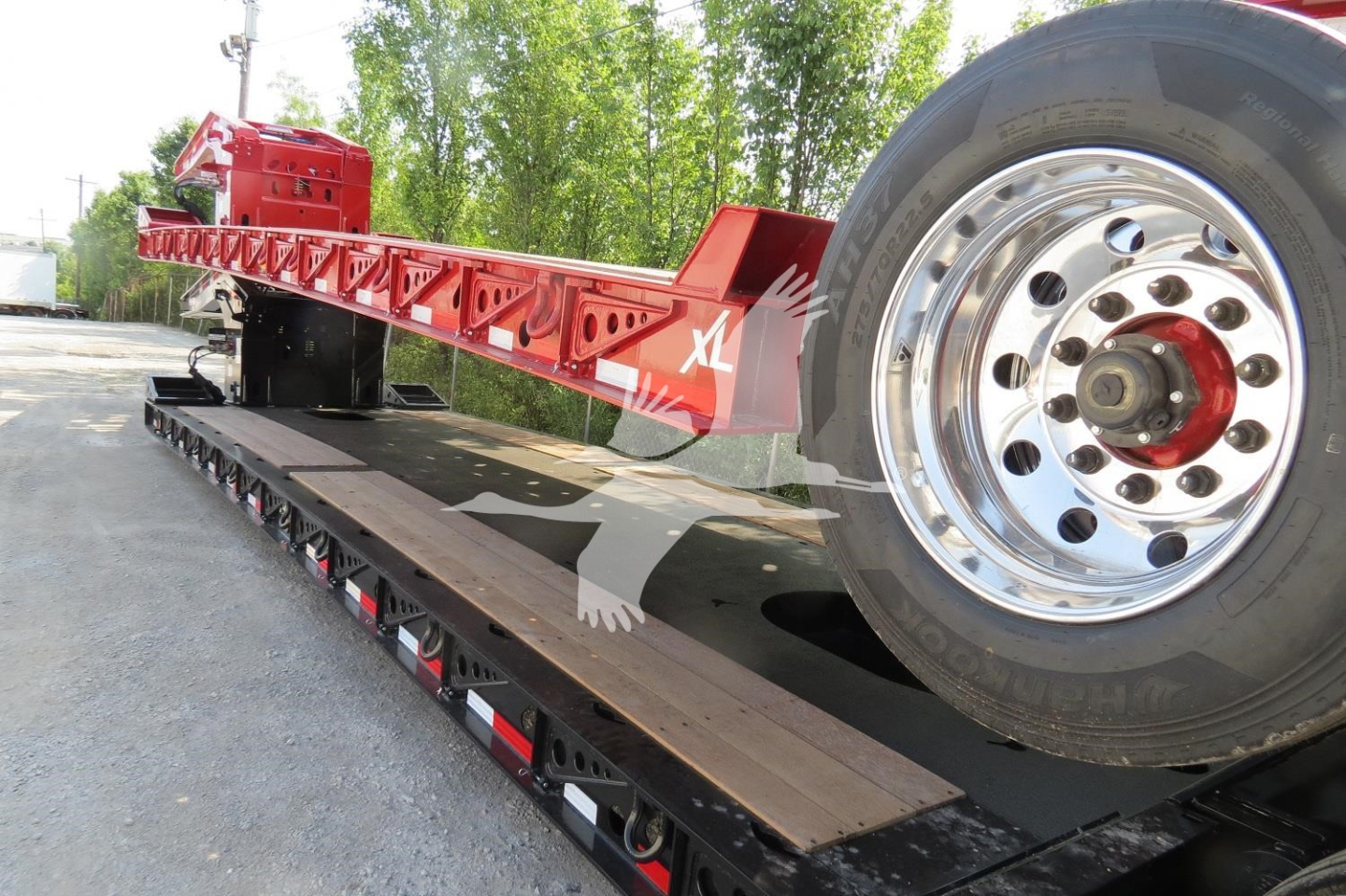 Lowboy trailer with a red XL Specialized 110Hdg-15 deck and a large wheel visible on the right, showing the trailer side rails and deck surface.