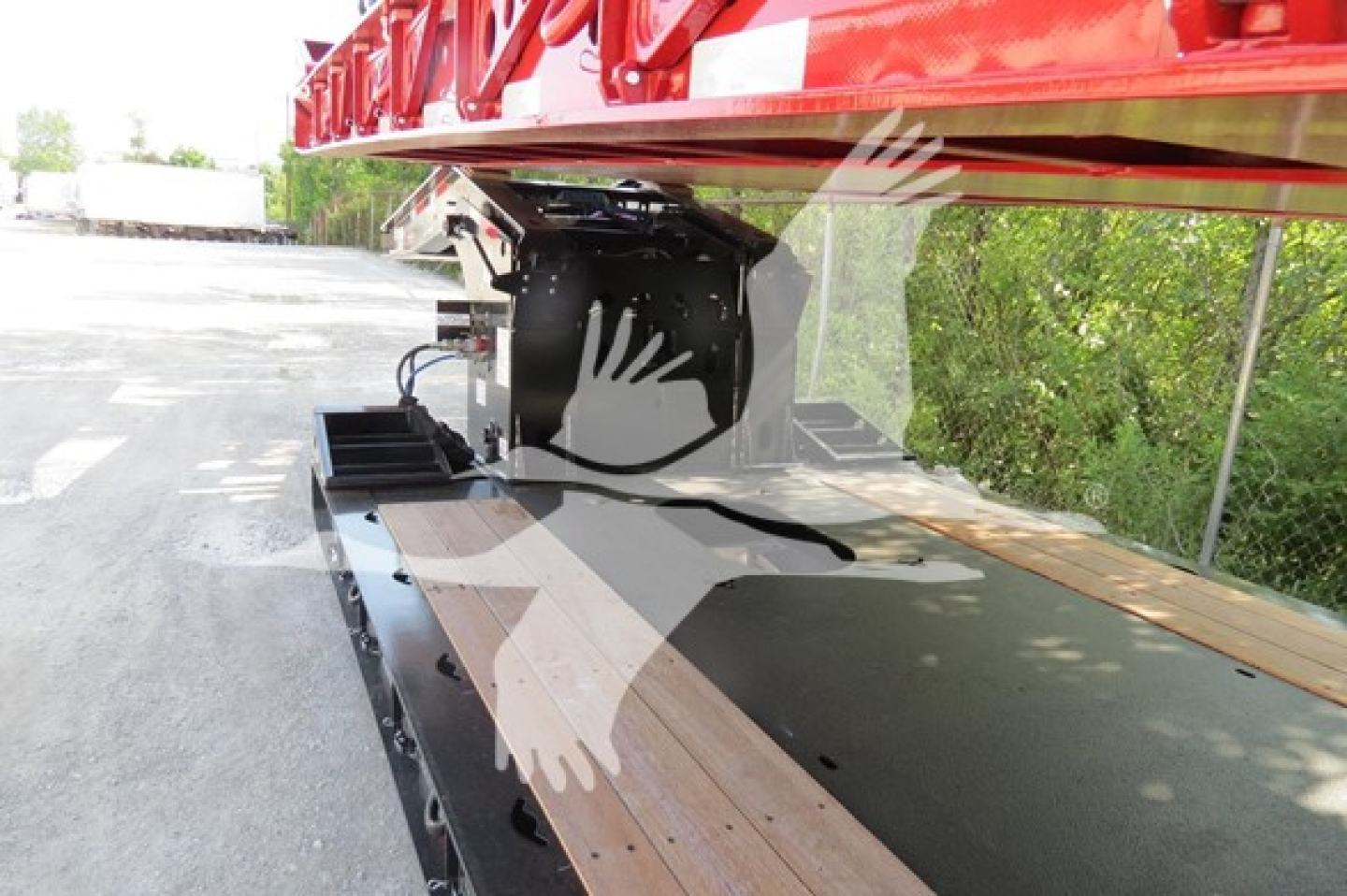 Trailer hitch area of a lowboy trailer showing mounting hardware and deck boards under a red elevated trailer component.