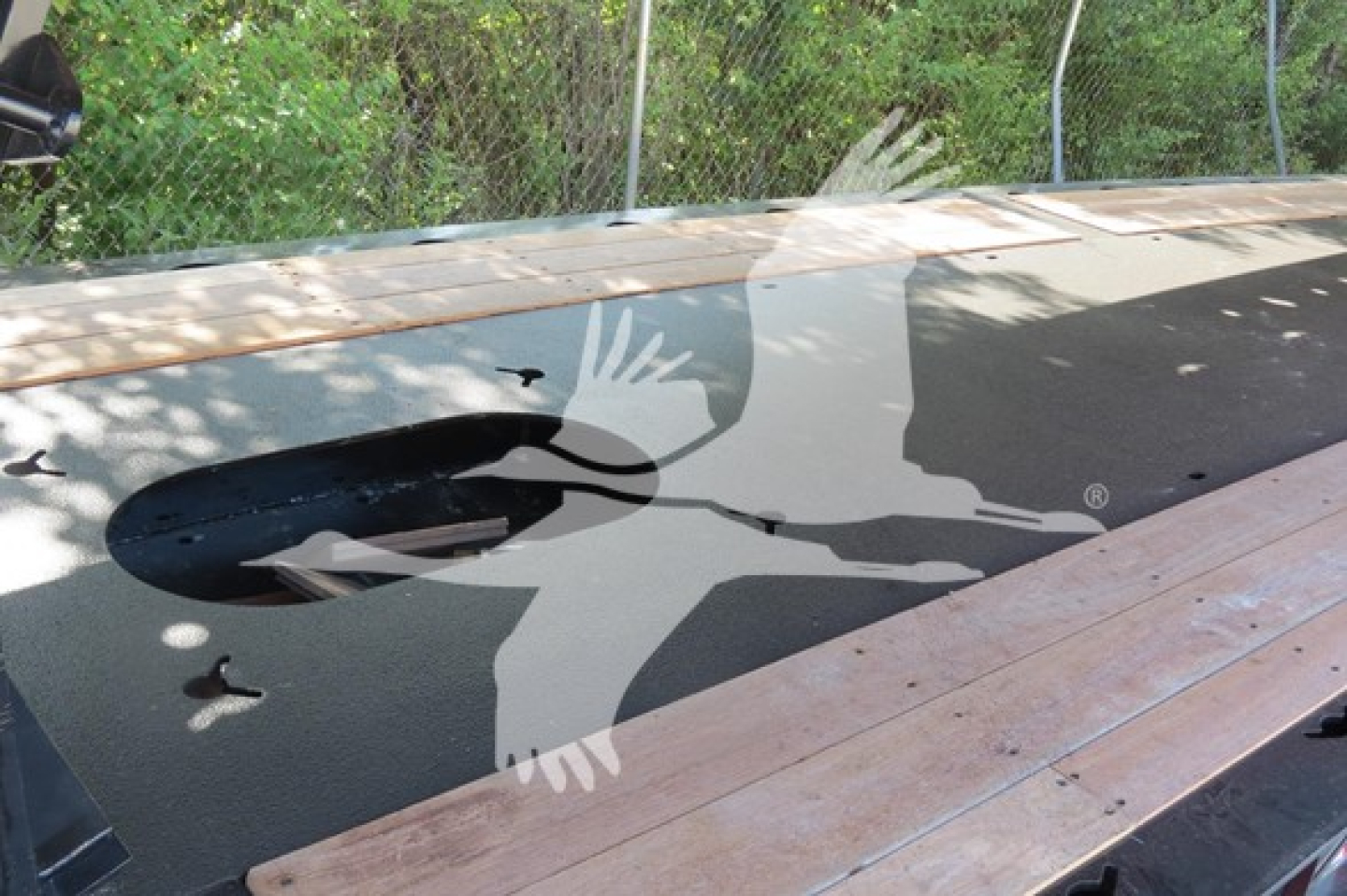 Trailer deck with large circular cutout and wooden planks; logo overlay of a bird silhouette on surface.
