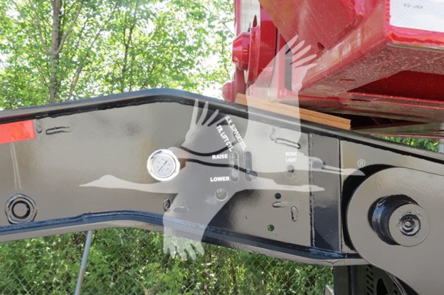 Trailer hitch/mounting frame with hydraulic controls and level indicators on a lowboy trailer. Visible labels show lower, raise, and work light indicators along with a round gauge on a black metal frame.