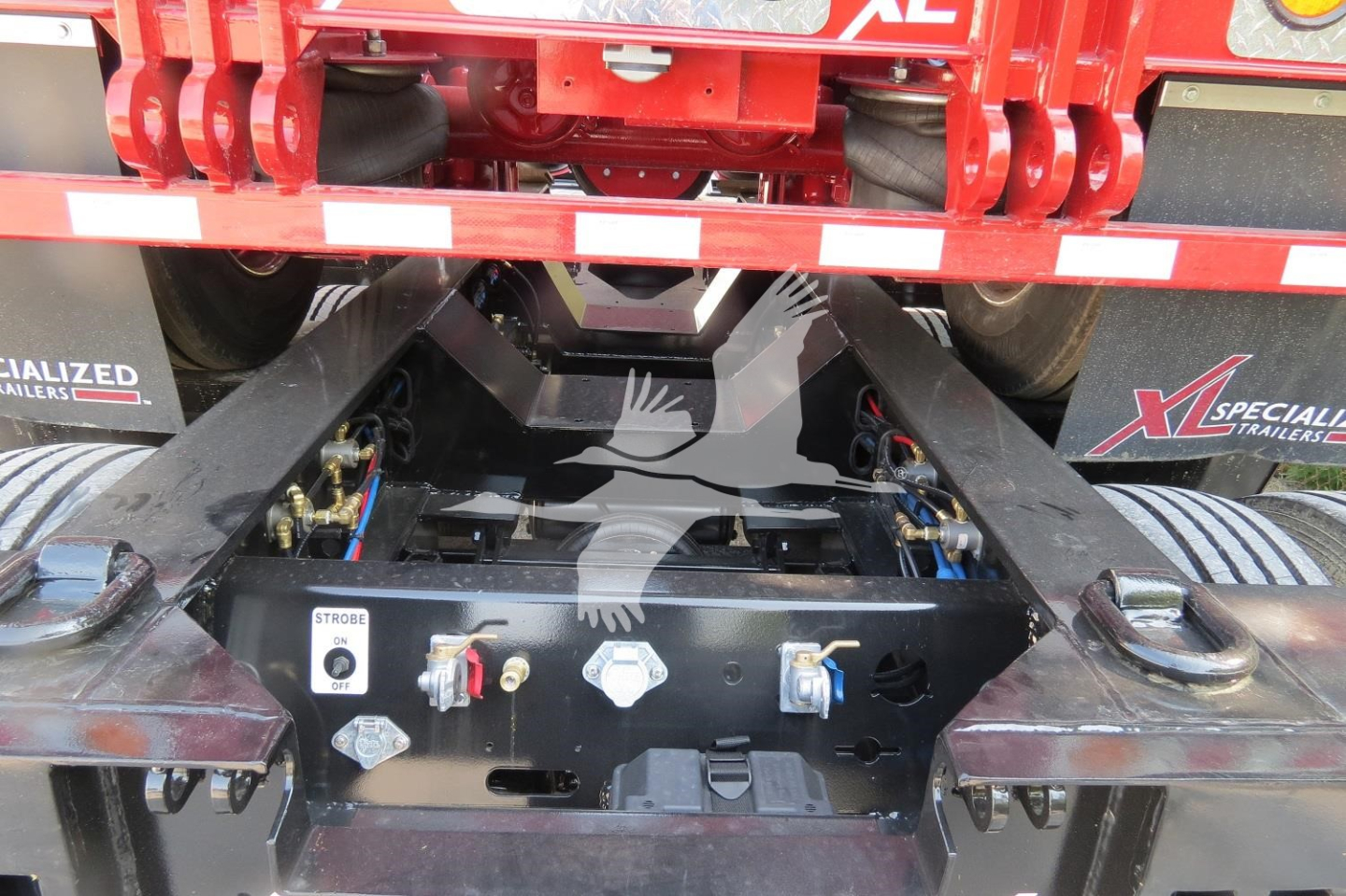 Trailer hitch assembly on a XL Specialized lowboy trailer showing hydraulic lines, valve blocks, and mounting hardware with stock decals.