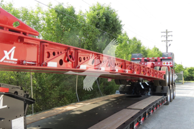 Red XL Manchester lowboy trailer frame showing transport equipment and dual rear axles in the image.