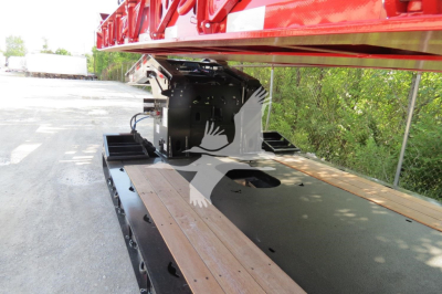 Trailer deck with a red elevated loading ramp on a lowboy trailer showing structural bracket and wood deck planks.