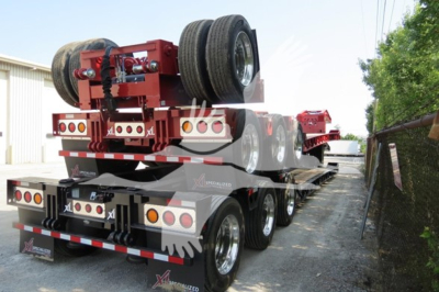 Trailer rear view showing twin front axle of xl specialized 110hdg-15 lowboy trailer with spare tires and red frame and reflective safety decals.