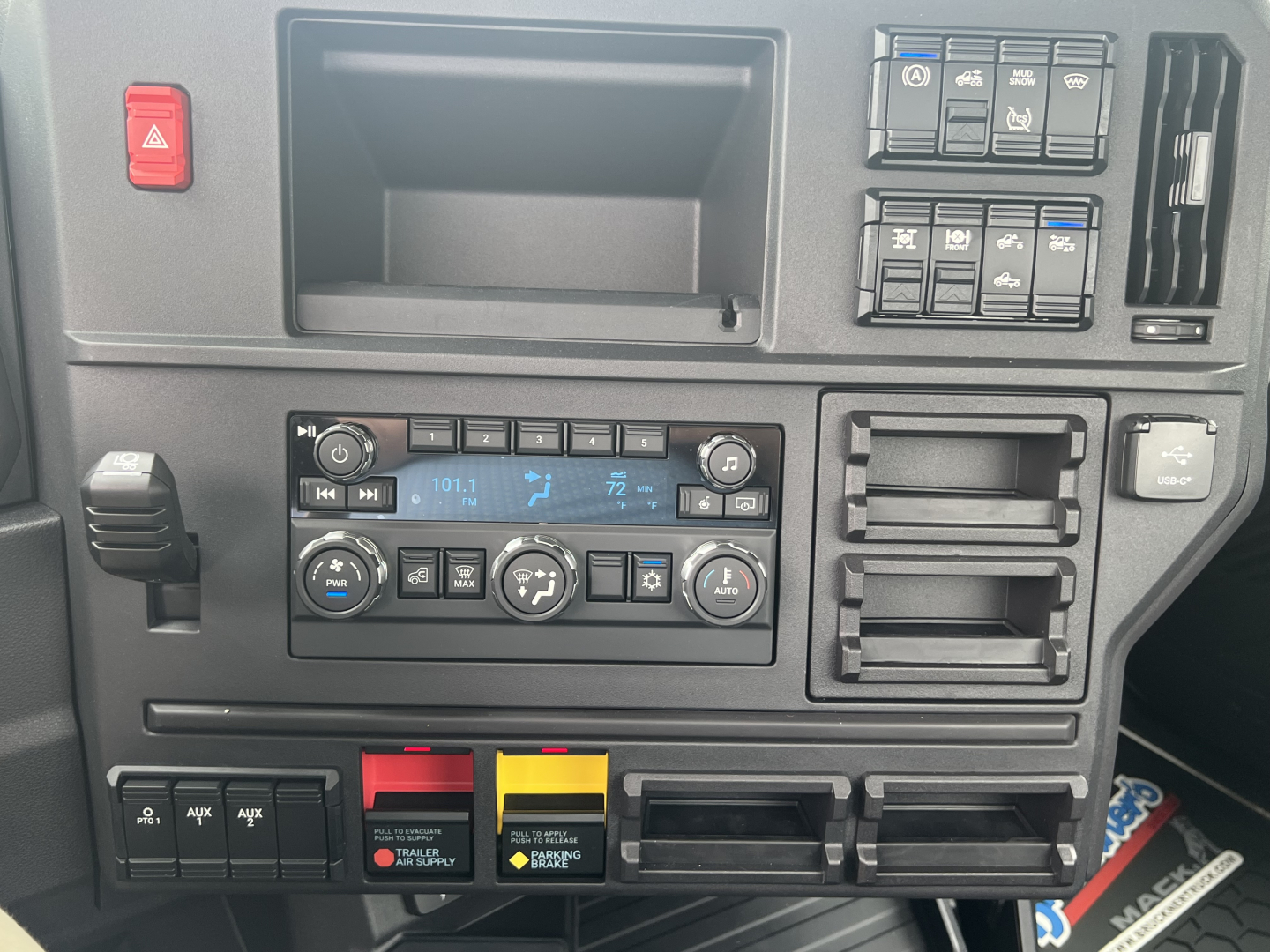 Truck cab dashboard showing climate controls, switches, and storage compartments in a Mack AN64T interior.