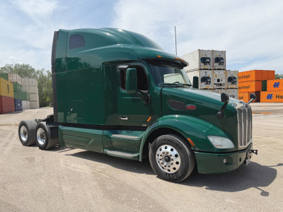 Green 2019 Peterbilt 579 conventional sleeper truck in a yard, side view showing cab, wheels, and long chassis with containers in background.