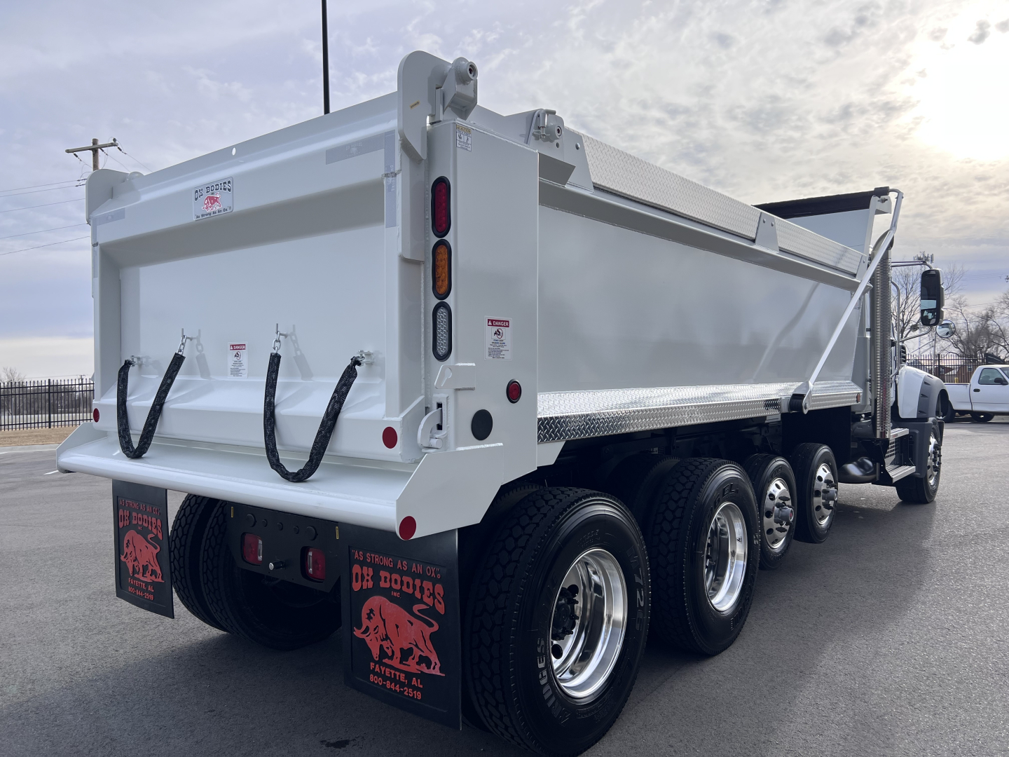 Dump truck rear and side view showing white Mack GR64F dump body with dual rear suspension and three axles, stock number 70374, VIN 1M2GR4GC3TM053862.