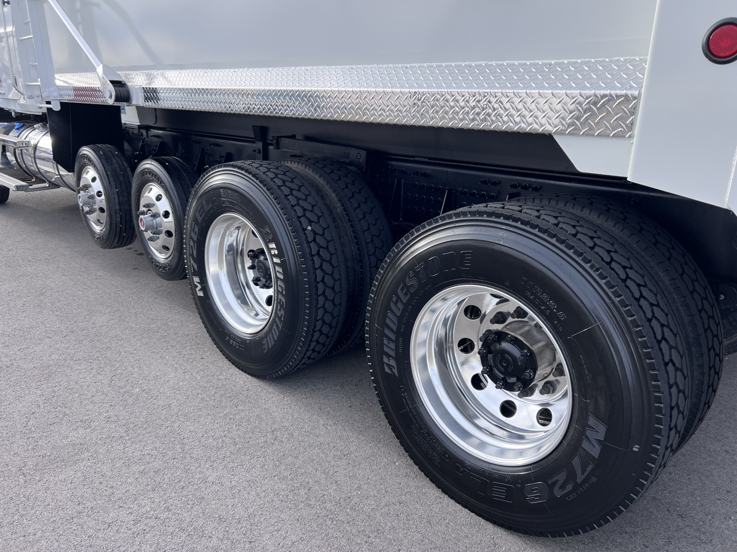 Dump truck wheels and axles showing multiple tires and chrome rims under a Mack GR64F dump body.