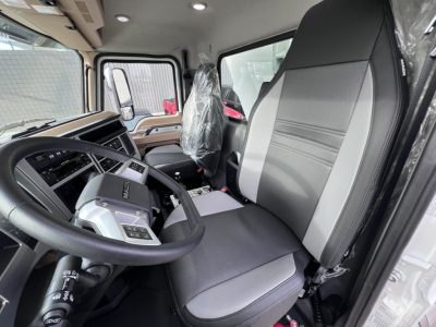 Cab interior of a 2026 Mack GR64F dump truck showing steering wheel, driver seat with plastic cover, and dashboard text.
