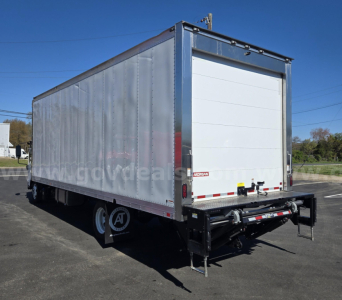 Isuzu NPR box truck trailer showing rear roll-up door, chrome trim, and black underride hitch. Visible label and small decals on rear door; wheel and dual tires visible.