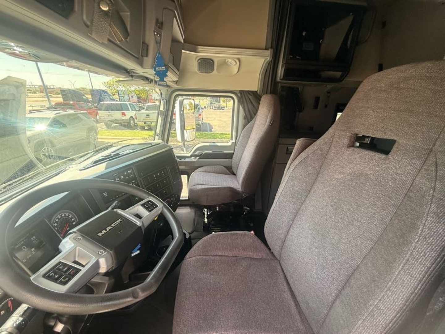 Interior of a 2020 Mack Anthem truck cabin with steering wheel, driver's seat, and passenger seat visible; dashboard and overhead storage; gray fabric seats and basic cabin controls.