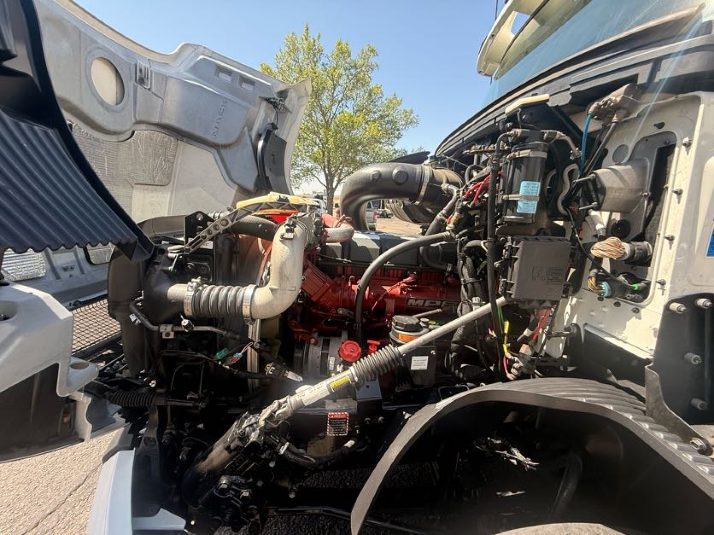 Mack ANTHEM engine bay with visible hoses, wiring, and a red engine block; no legible model text other than general truck components.
