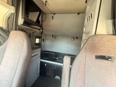 Cab interior of a 2020 Mack Anthem sleeper cab showing dashboard area, bunk bed behind driver seat, and storage compartments.