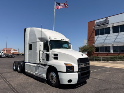 Mack Anthem semi truck in a dealership lot, white cab with sleeper, dual rear axles, and front grille with Mack logo.