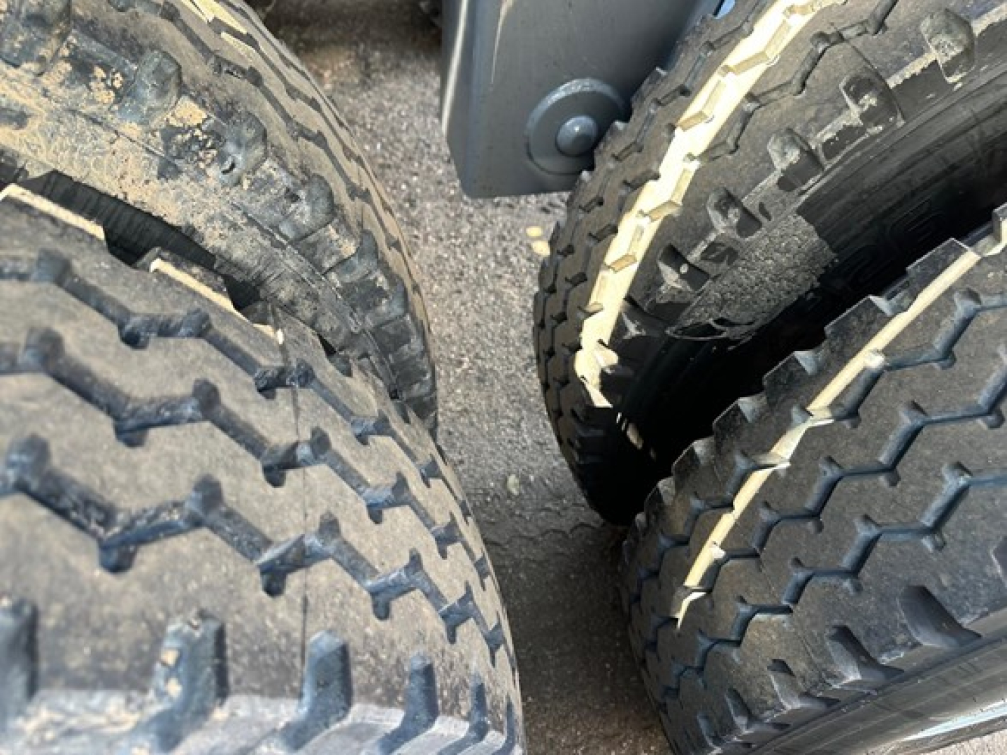 Dual rear tires of a dump trailer showing rugged tread and mud on the left tire with a lighter tread on the right; part of trailer frame visible.