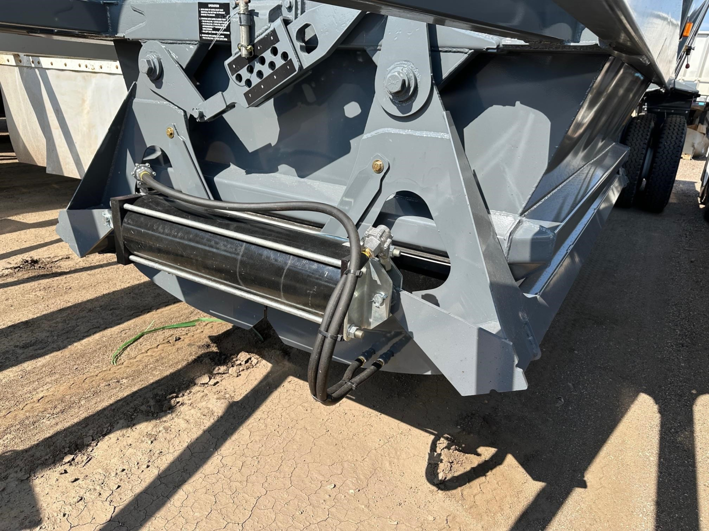 Dump trailer front hitch area showing hydraulic hose and roller mechanism, gray paint, heavy steel frame, and mounting brackets.