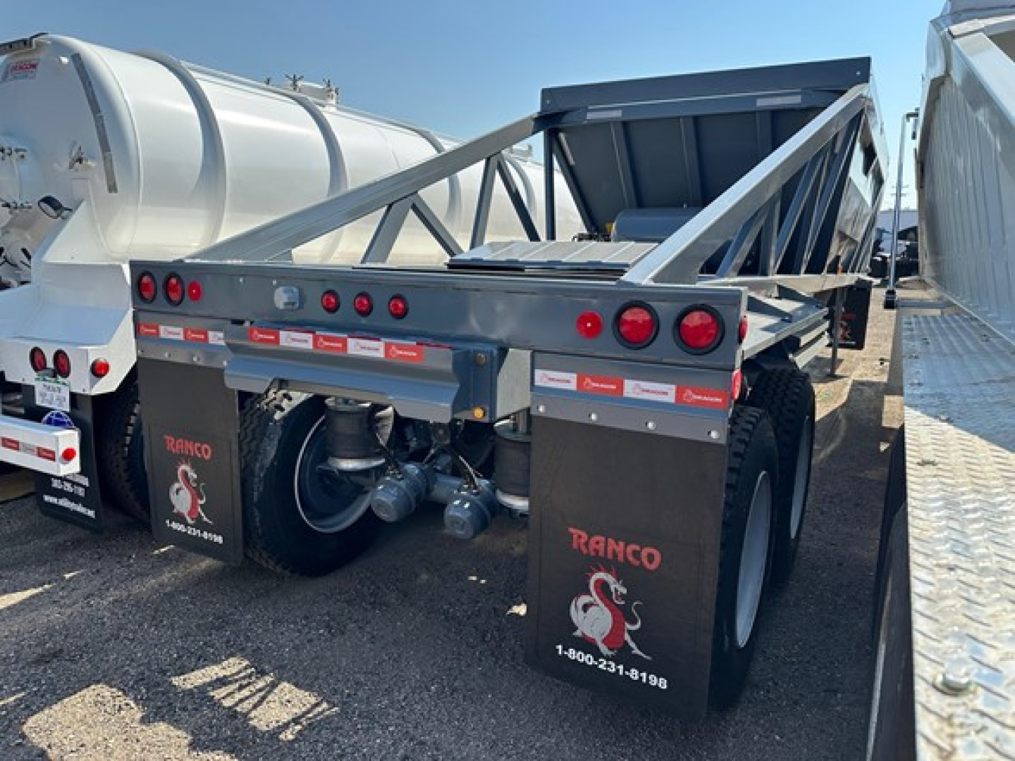 Ranco LW21-40 dump trailer showing rear view with 3 red taillights per side, dual axles, black mud flaps with Ranco logo and phone number, and warning labels along rear edge.