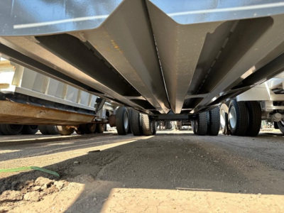 Underbelly view of a trailer showing structural beams and supports with wheel areas in background.